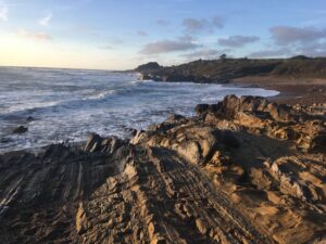 rocky terrain in the foreground with the ocean waves curving around the coast in the background